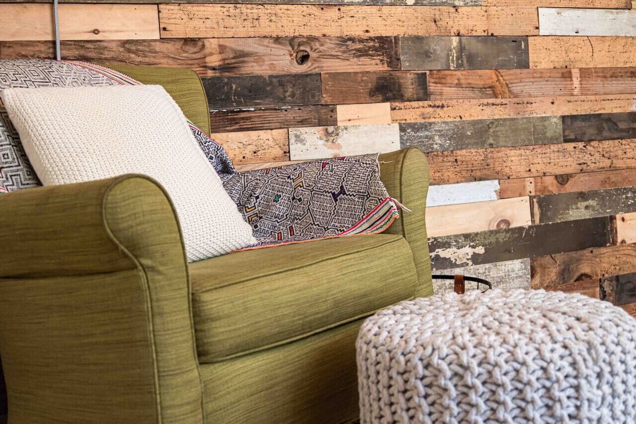 Un canapé vert avec des coussins à motifs, placé contre un mur en bois.