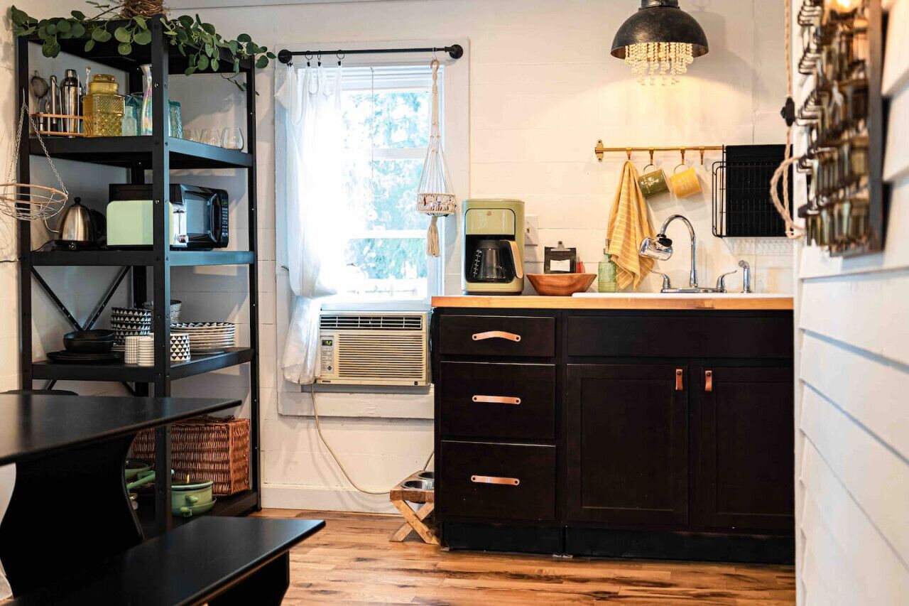 Een kleine keuken met een zwart aanrecht, een koffieapparaat en een hanglamp.