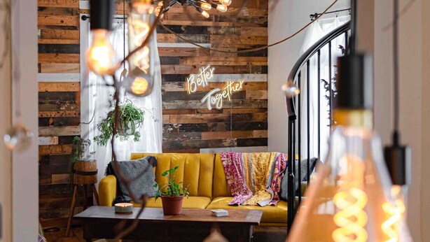 Un accogliente soggiorno con una parete in legno, un divano giallo, un tavolino da caffè e un neon con la scritta “Better Together”.