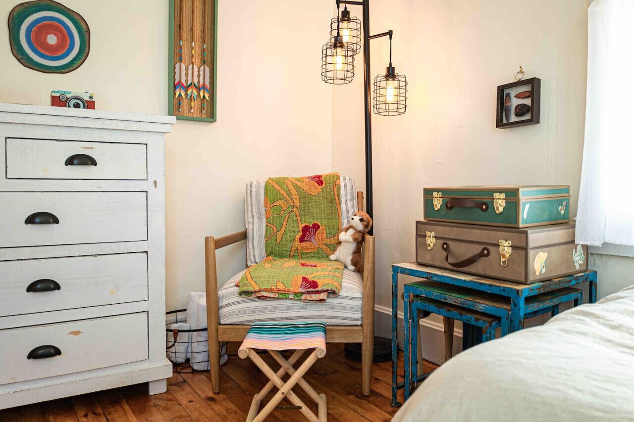 A cozy room with a wooden chair, a white dresser, and a small table with suitcases.