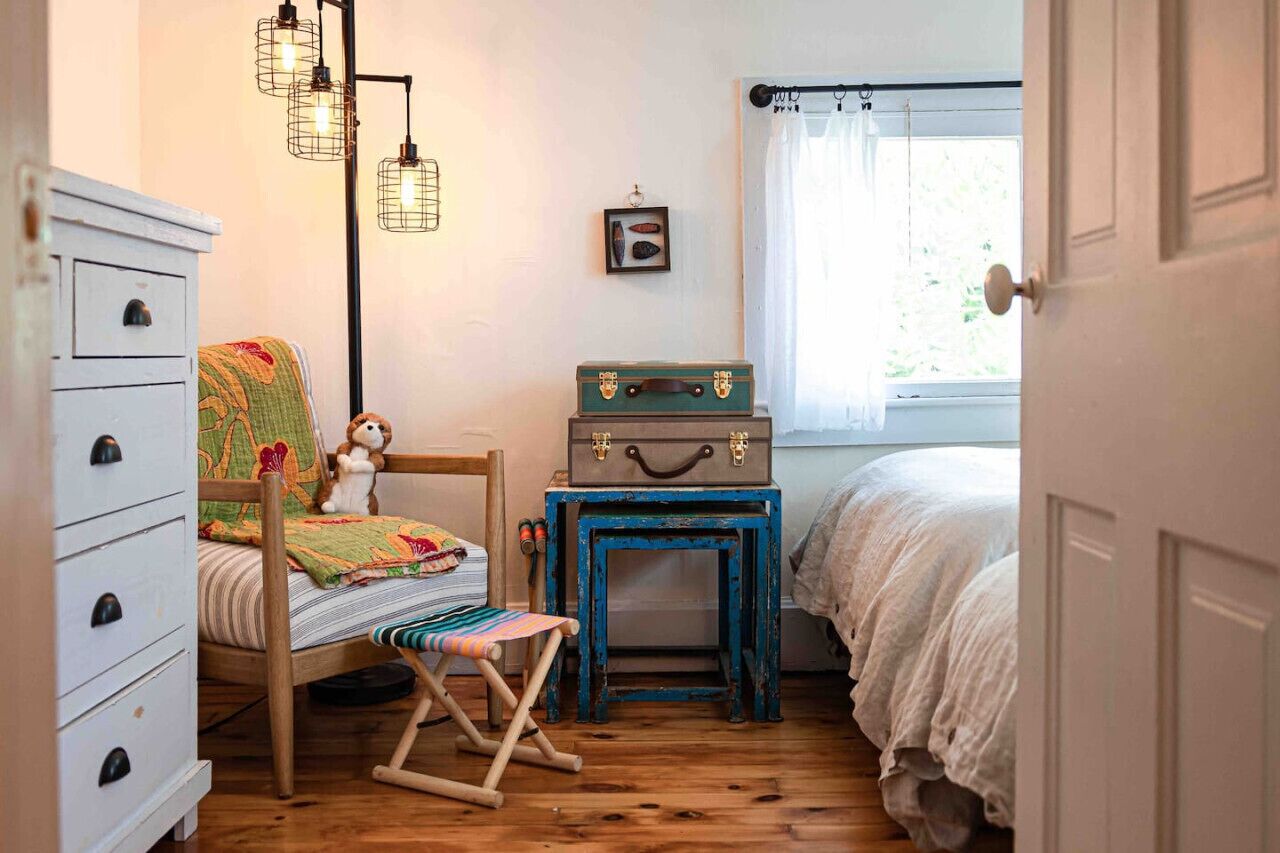 Un dormitorio acogedor con un aparador de madera, una silla, una mesita con maletas y una cama con ropa de cama blanca.