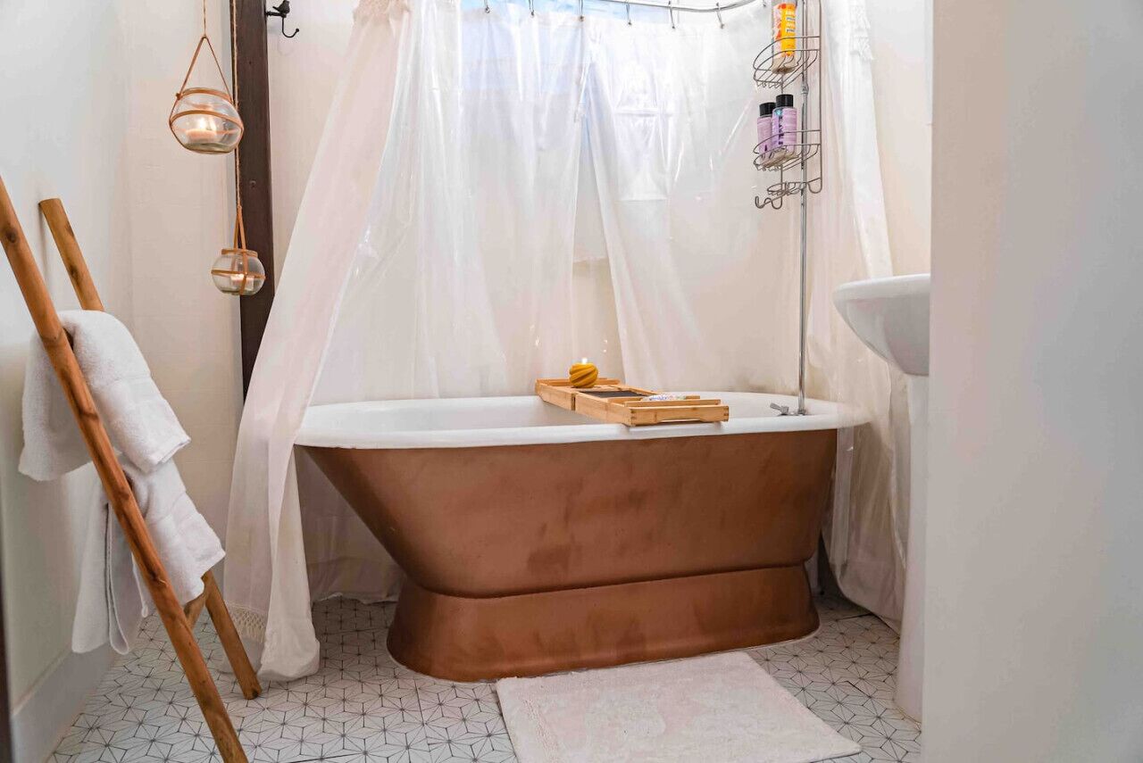 Une salle de bain avec une baignoire sur pieds, un porte-serviettes en bois, un rideau de douche blanc et une étagère contenant des articles de toilette.