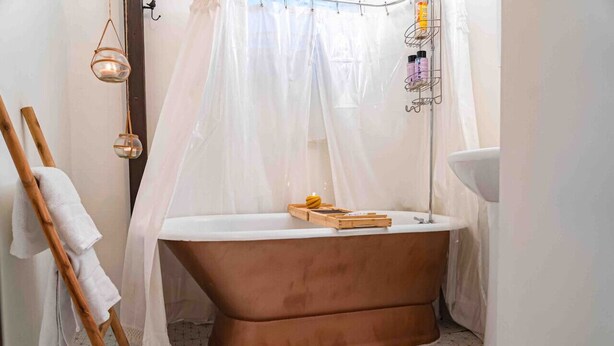 A bathroom with a freestanding bathtub, a wooden towel rack, a white shower curtain, and a shelf with toiletries.