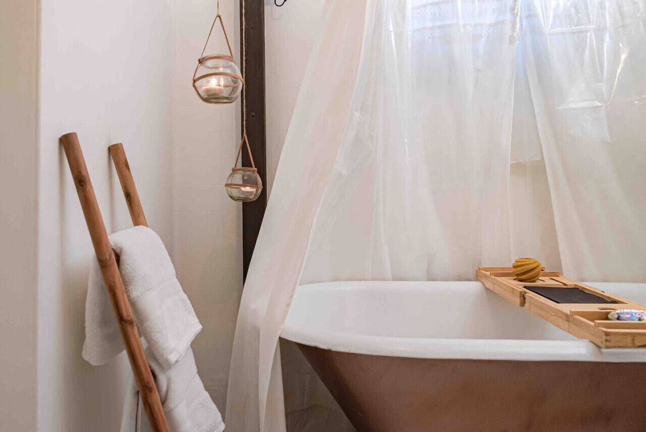 A bathroom with a bathtub, a wooden towel rack, a glass candle holder, and a wooden tray with a book and a small object.