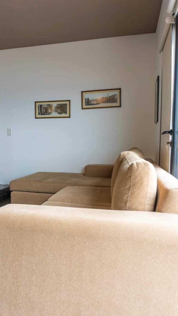 A living room with a beige sofa, two framed pictures on the wall, and a door to the right.