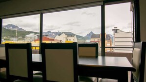 A dining area with a table and chairs, large windows with a view of buildings and mountains. - Cumbre (Ushuaia)