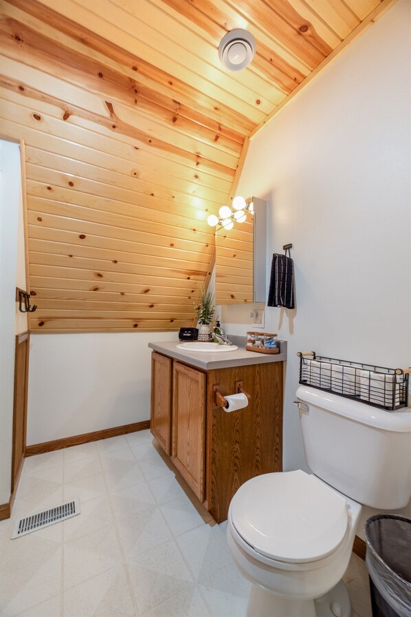 A small bathroom with a wooden ceiling, a toilet, a sink with a towel rack, and a mirror.