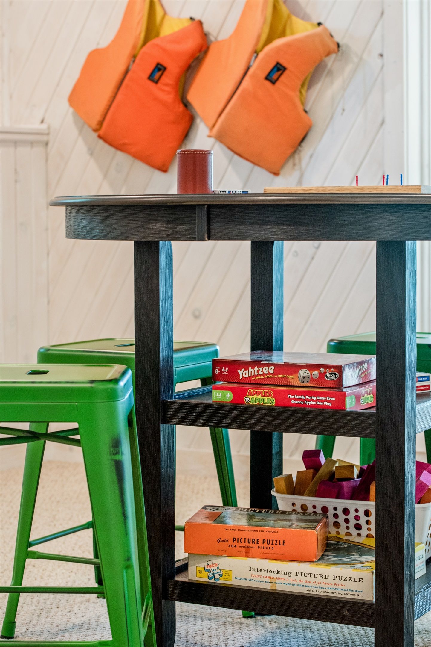 A wooden table with a black top, green chairs, and various board games and puzzles.