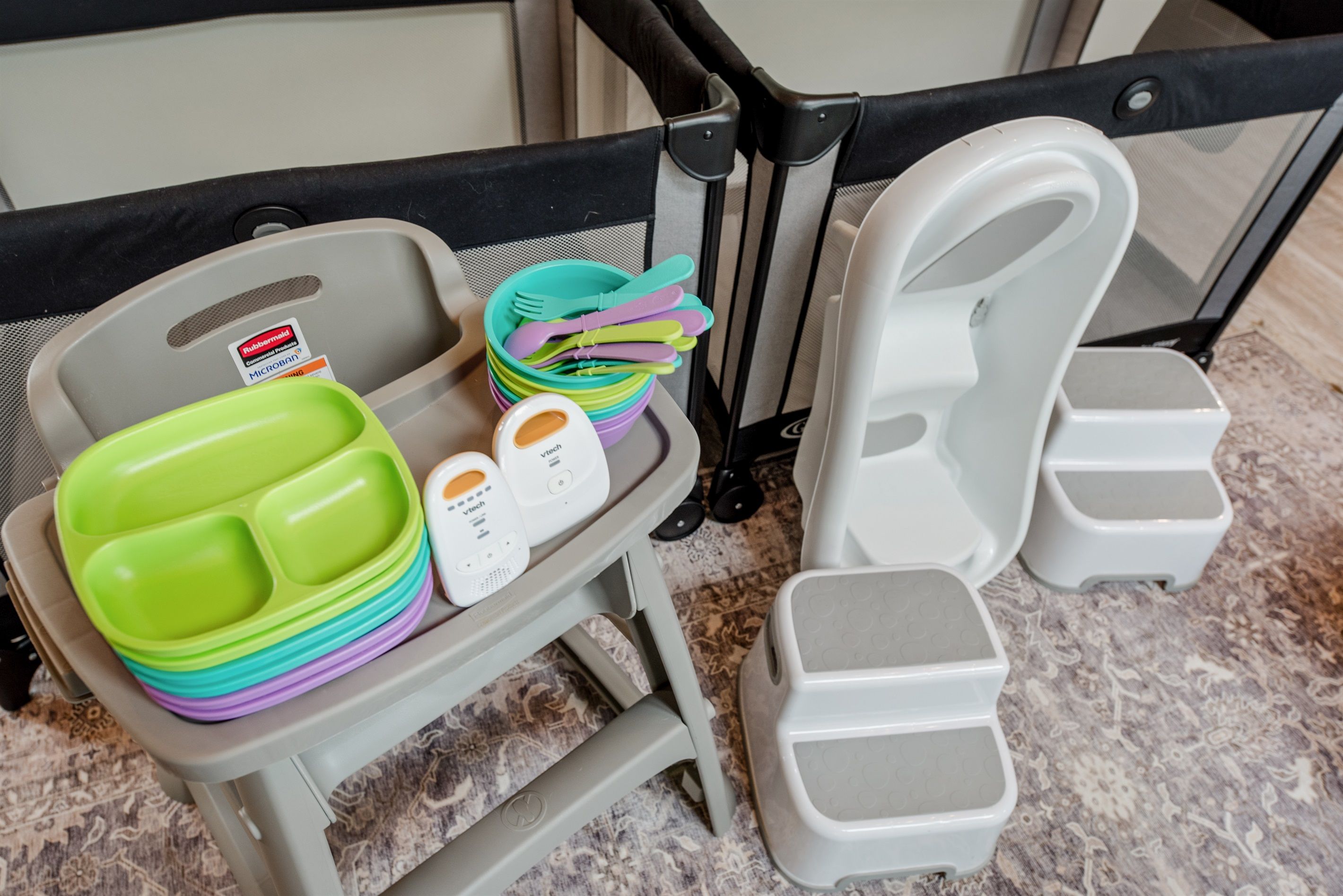 Un chariot de voyage contenant une pile de boîtes en plastique de couleurs vives, un appareil blanc et une paire de pantoufles blanches.