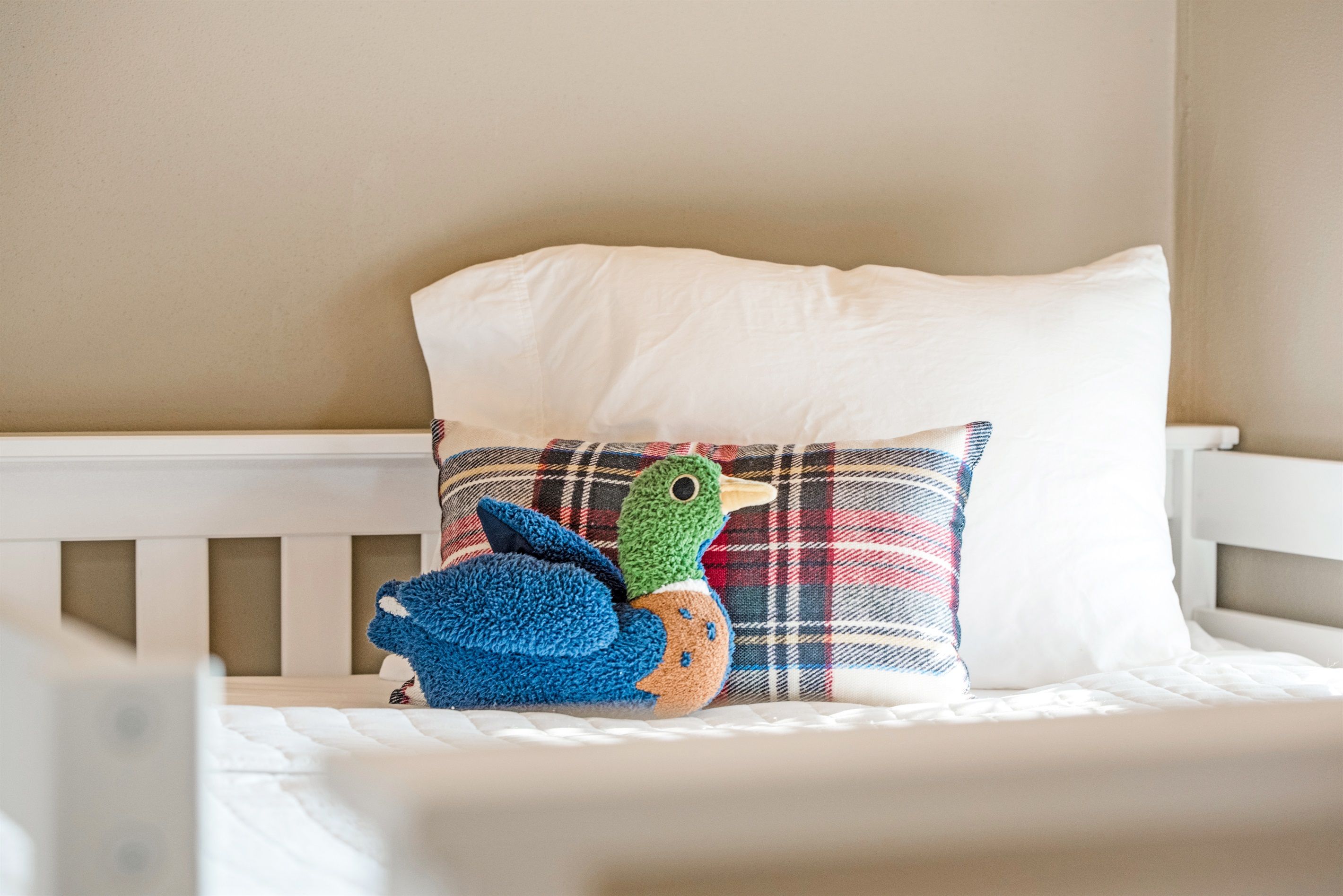 A crib with a white mattress, a white pillow with a plaid pattern, and a plush duck toy.