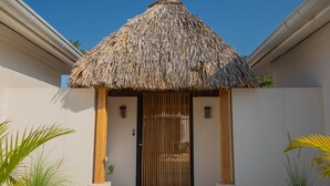 A thatched-roof entrance with a wooden gate, flanked by palm plants, leading to a building with a white exterior and a wooden door frame. - Modern Villa 2 bedrooms- PetFriendly Beautiful Kitchen Pool close to beaches (Guanacaste Province)
