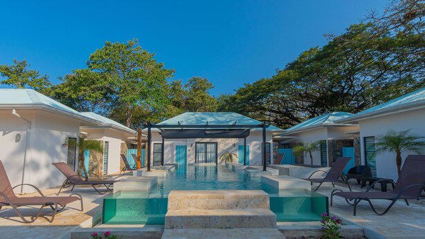 A swimming pool with steps leading to the water, surrounded by lounge chairs and a covered area. - Modern Villa 2 bedrooms- PetFriendly Beautiful Kitchen Pool close to beaches (Guanacaste Province)