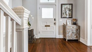 A hallway with a white door, a wooden cabinet with a picture, and a staircase with white columns. - Historic Oasis. Heated pool, Historic Oasis. Heated pool spa large backyard (Galveston)