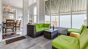 A cozy living room with wicker furniture, a dining area with wooden chairs, and large windows with a view of the outside. - Historic Oasis. Heated pool, Historic Oasis. Heated pool spa large backyard (Galveston)