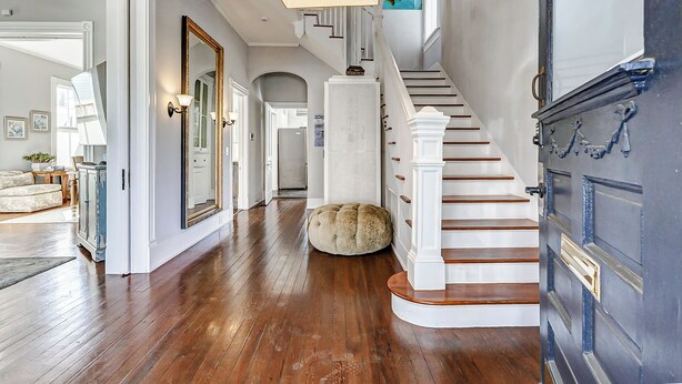 A spacious hallway with a wooden floor, a round ottoman, a staircase with white railings, and a large mirror on the wall. - Historic Oasis. Heated pool, Historic Oasis. Heated pool spa large backyard (Galveston)