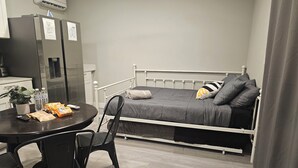Une pièce de taille modeste comprenant un lit, une petite table, des chaises, un réfrigérateur et une plante en pot.