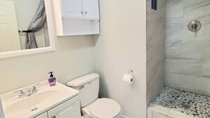 Une salle de bain avec un lavabo blanc, des toilettes, une douche avec un mur en marbre et un miroir au-dessus du lavabo.