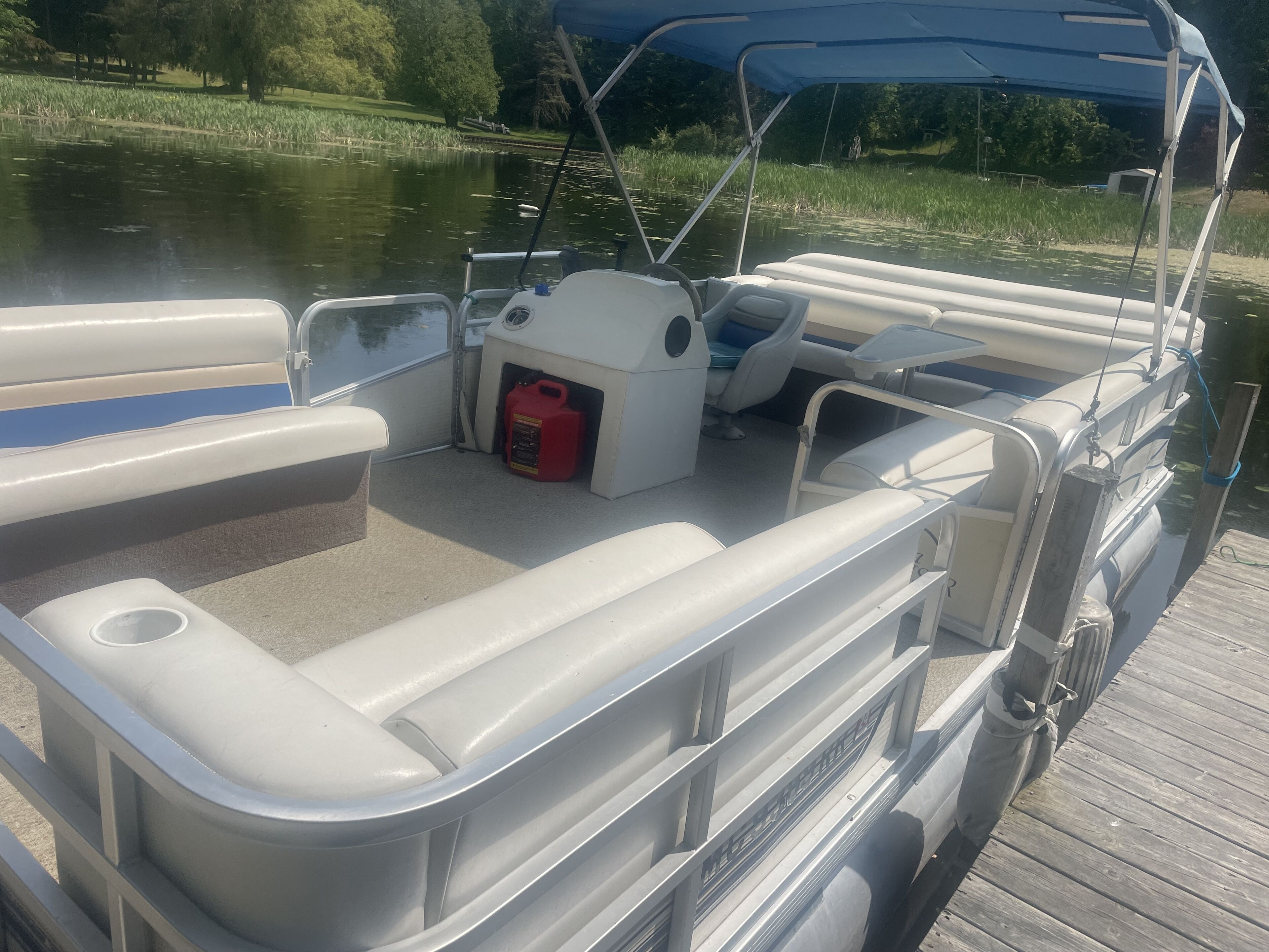 A boat with a covered seating area, a fuel container, and a wooden dock.