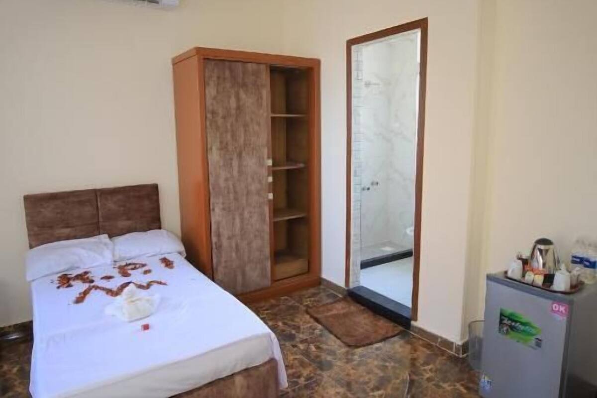 Ein Hotelzimmer mit Bett, Schrank, Spiegel und einem kleinen Tisch mit Kühlschrank.