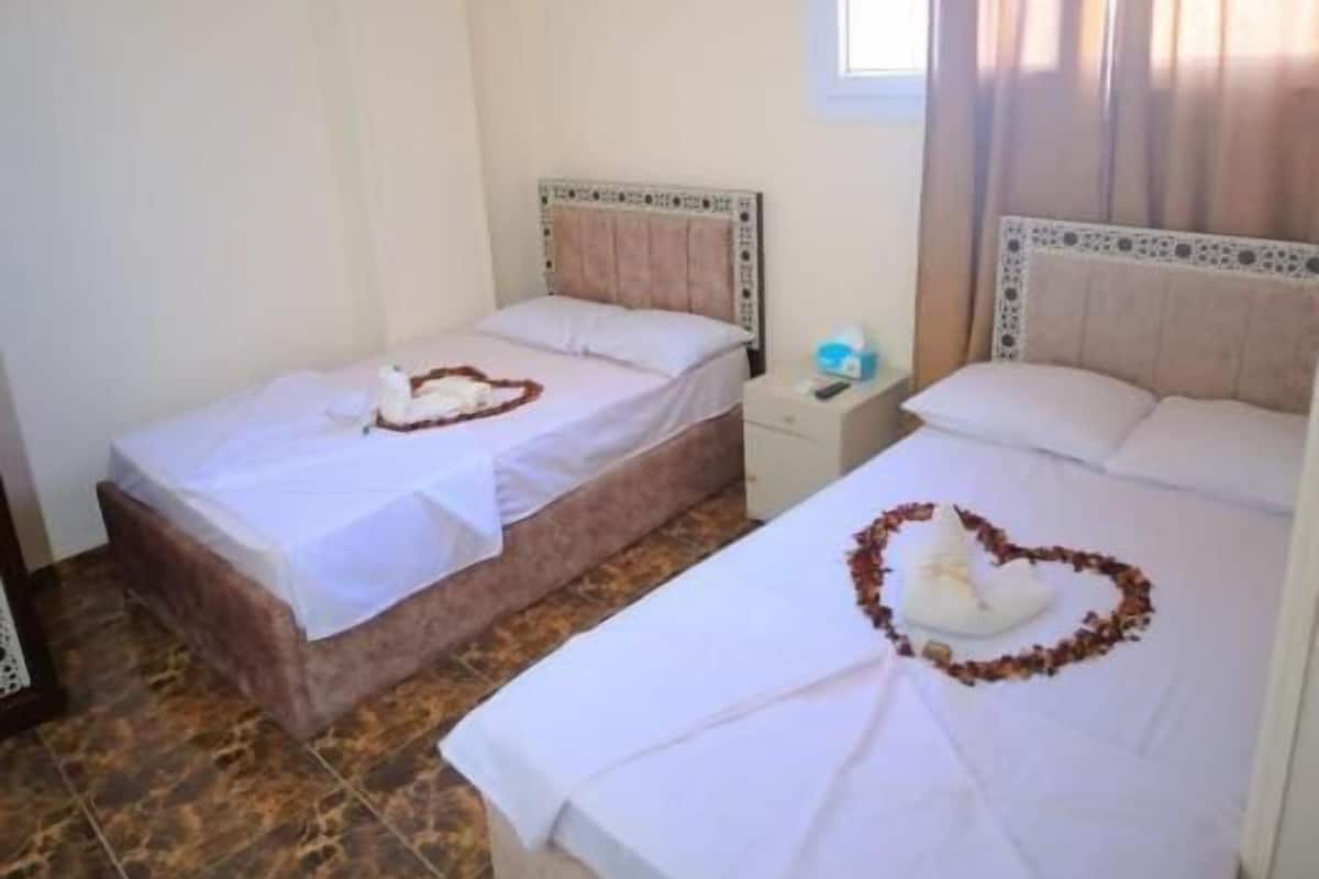 Ein Hotelzimmer mit zwei Betten, einem Fenster mit Vorhängen und einem kleinen Nachttisch.