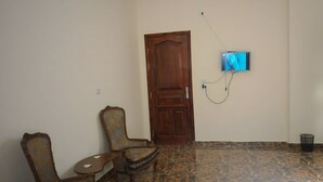 Una habitación con puerta de madera, televisor montado en la pared y dos sillas.