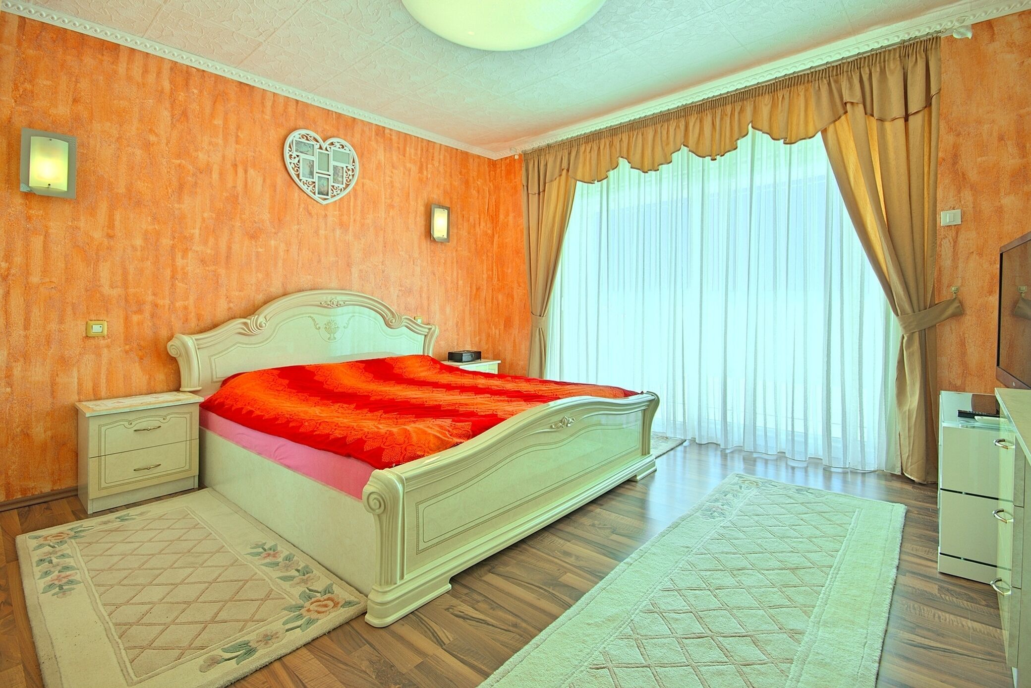 A bedroom with a bed, nightstands, a dresser, and a window with curtains.