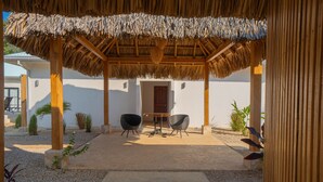 A covered outdoor seating area with two chairs and a table, surrounded by a gravel path and small plants. - Perfect Studio Kitchen Beautiful Pool Close to beach Avellanas AC PetFriendly (Guanacaste Province)