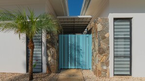 A modern building with a stone facade, a blue gate, and a palm tree. - Perfect Studio Kitchen Beautiful Pool Close to beach Avellanas AC PetFriendly (Guanacaste Province)