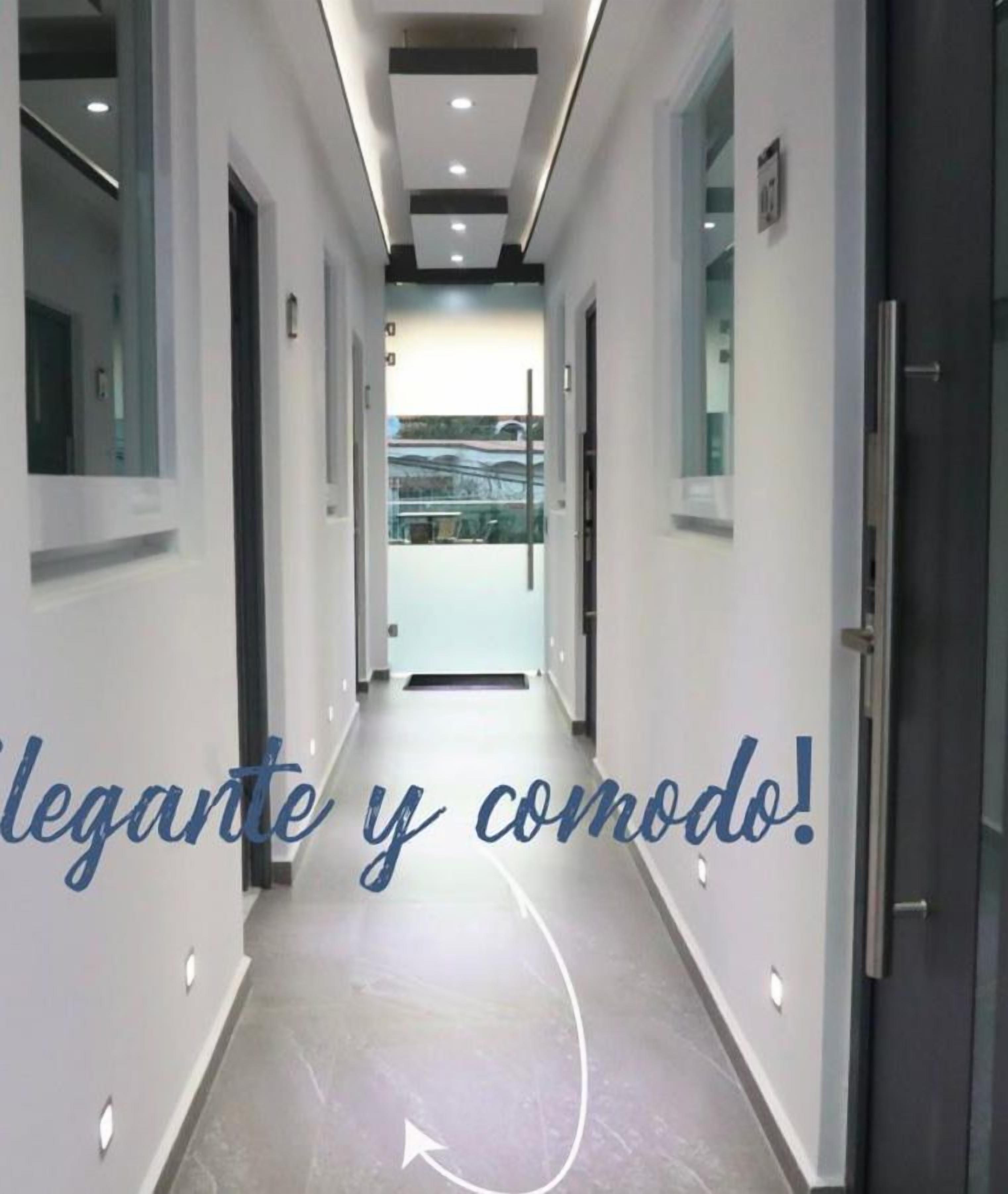 Un pasillo de hotel de diseño moderno, con una larga galería de puertas a ambos lados que conduce a una habitación luminosa al final.