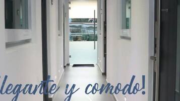 Un pasillo de hotel de diseño moderno, con una larga galería de puertas a ambos lados que conduce a una habitación luminosa al final.