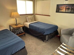 A room with two beds, a chair, a nightstand, and a picture on the wall.