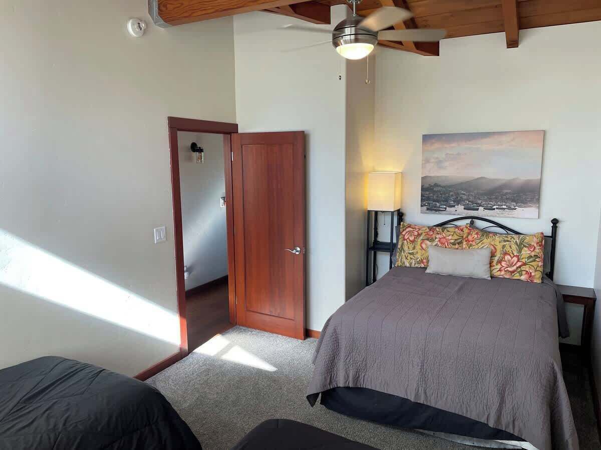 A bedroom with a bed, a nightstand, a lamp, a door, and a painting on the wall.