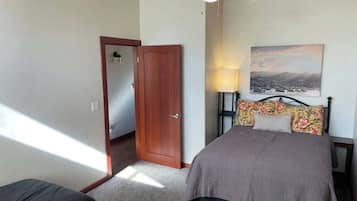 A bedroom with a bed, a nightstand, a lamp, a door, and a painting on the wall.