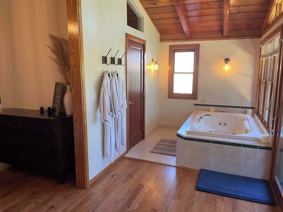 A bathroom with a wooden floor, a bathtub, a vanity with a mirror, and a towel rack with robes.