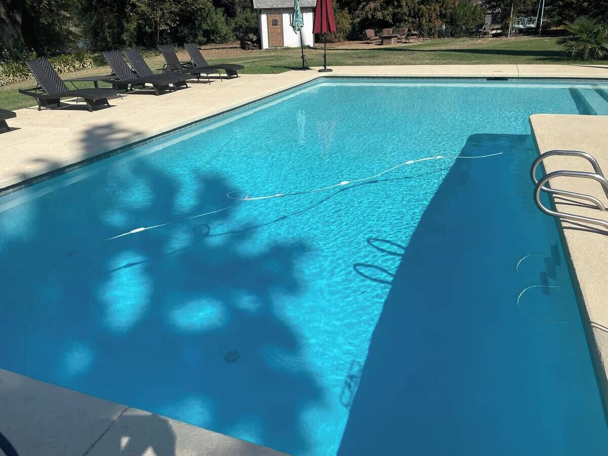 Ein rechteckiger Swimmingpool mit klarem, blauem Wasser, umgeben von Liegestühlen und ein kleines Gebäude im Hintergrund.
