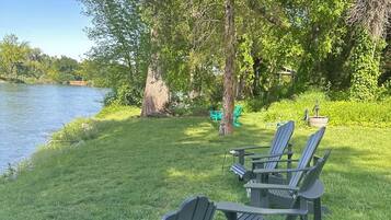 A lakeside outdoor seating area with Adirondack chairs and a table.