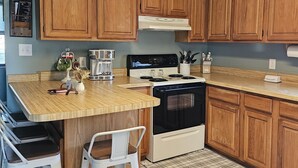 A kitchen with wooden cabinets, a central island with stools, a stove, and a microwave. - Private Home and Dock on Dunns Creek!
Sportsman's paradise, hosted by Sportsman. (Satsuma)