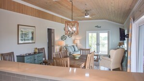 A spacious living area with a wooden ceiling, a dining table with chairs, a sofa, and a television.