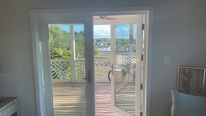 A room with a sliding glass door leading to a wooden deck with a view of a landscaped area and a building in the distance.