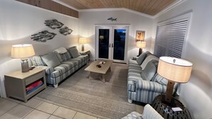 A living room with two sofas, a coffee table, and lamps. There is a ceiling fan and a wall-mounted decoration.