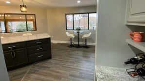 Una cocina moderna con armarios oscuros, una encimera de mármol y una zona de comedor con dos sillas blancas y una mesa pequeña.