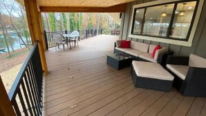 Un espacio de estar al aire libre techado con cubierta de madera, sofá y una mesa.