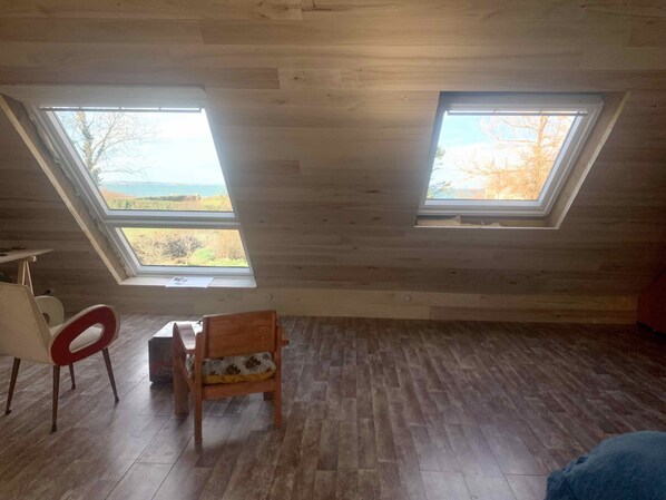 A room with a sloped ceiling, two skylights, a wooden floor, a white chair, and a small table.