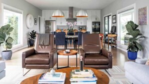 A modern living room with leather sofas, a coffee table, and a dining area with a kitchen in the background.