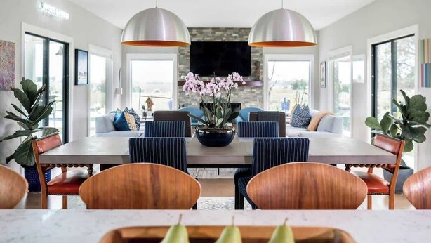 A modern dining area with a large table, striped chairs, and pendant lighting.