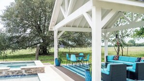 A covered outdoor area with a pool, seating, and a view of a grassy field.