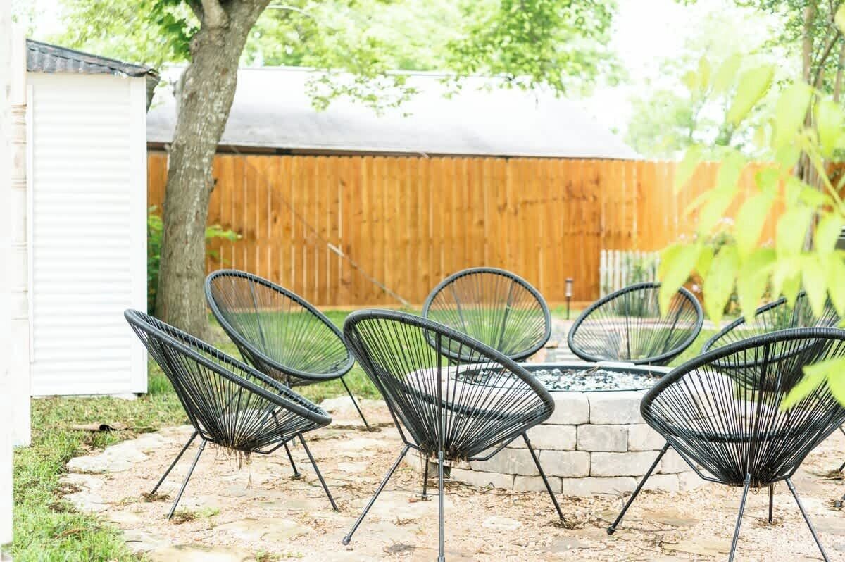 Un espace patio aménagé avec quatre chaises en fil de fer noir disposées autour d’un foyer en pierre.