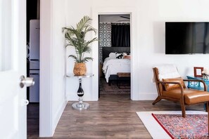 Hotelkamer met een bed, een aan de muur bevestigde televisie, een kamerplant, een stoel en een tafeltje.