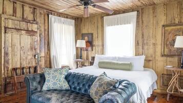 Une pièce rustique avec un grand lit, un canapé bleu, des murs en bois et un ventilateur de plafond.