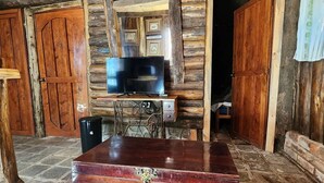 A rustic wooden cabin interior with a television on a wooden stand, a chest of drawers, and stone flooring. - Cabaña Pipil en Los Naranjos (Los Naranjos)
